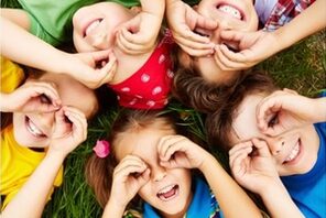 Lachende Kinder liegen Kopf an Kopf im Kreis auf einer Wiese. © Freepik