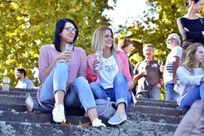Zwei junge Frauen mit Weingläsern auf Stufen am Rheinufer © Die Mainzer Winzer e.V./ Uwe Feuerbach
